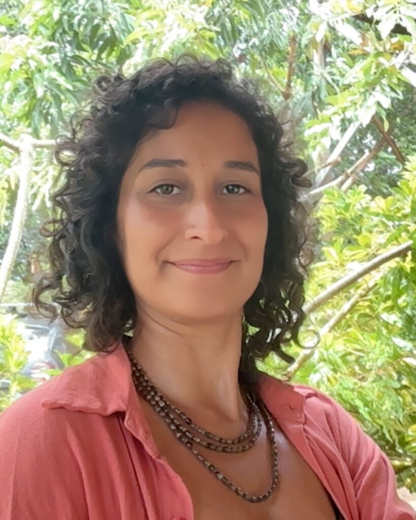 Renata Bozza Gomez, psicóloga, de blusa rosa, em frente a vegetação.